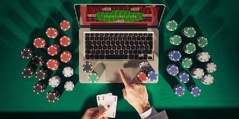 man playing online poker on a laptop computer with chips stacked around the table